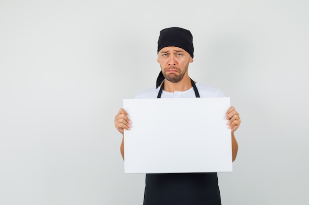 Baker man holding empty canvas in t-shirt, apron and looking sad.