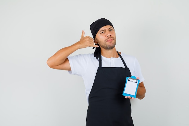 Baker man holding mini clipboard, showing phone gesture in t-shirt