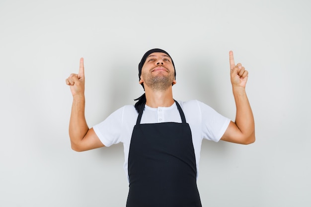 Baker man pointing fingers up in t-shirt, apron and looking grateful.