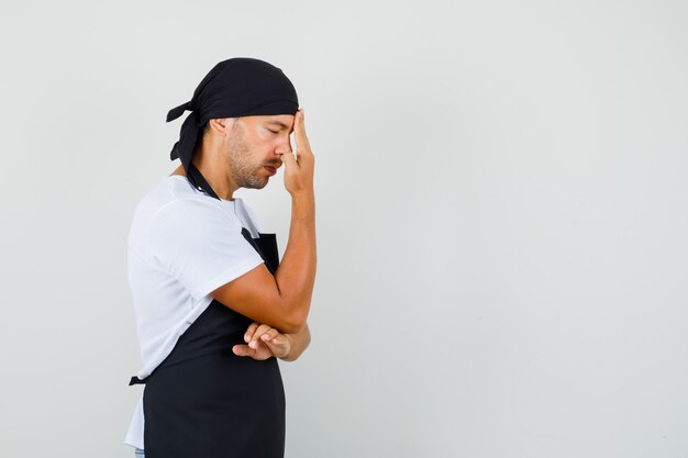 Baker man rubbing forehead in t-shirt, apron and looking exhausted