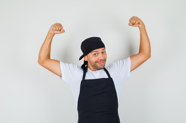 Baker man showing his muscles in t-shirt, apron and looking cheerful.