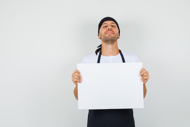 Baker man in t-shirt, apron holding empty canvas and looking proud