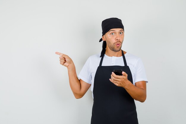 Baker man in t-shirt, apron holding mobile phone