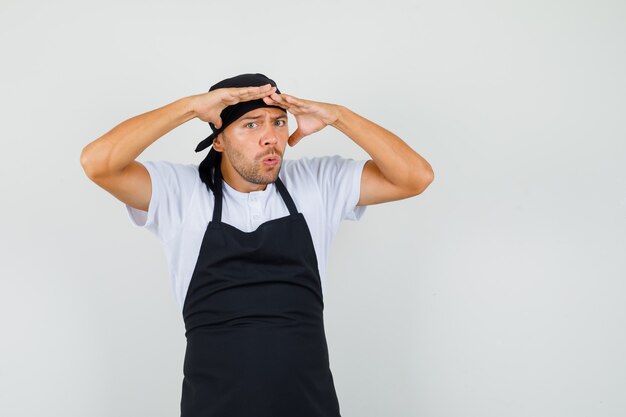 Baker man in t-shirt, apron looking far away with hands over head