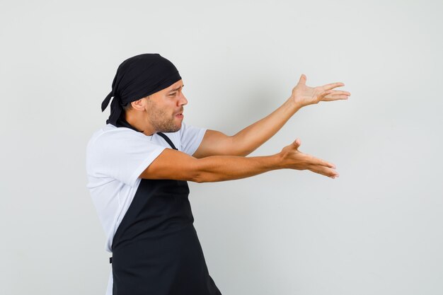 Baker man in t-shirt, apron making asking question gesture and looking nervous