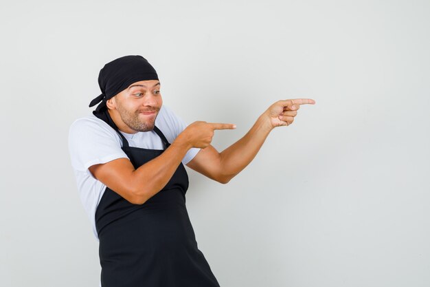 Baker man in t-shirt, apron pointing to the side and looking frisky