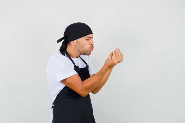 Baker man in t-shirt, apron showing italian gesture and pouting lips