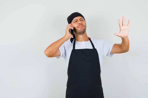 携帯電話で話しているベイカーの男、Tシャツで停止ジェスチャーを示しています