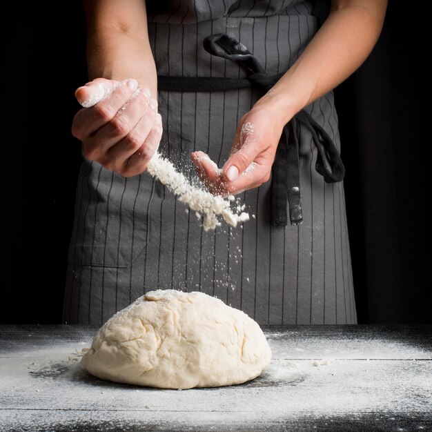 Baker pouring flour over dough