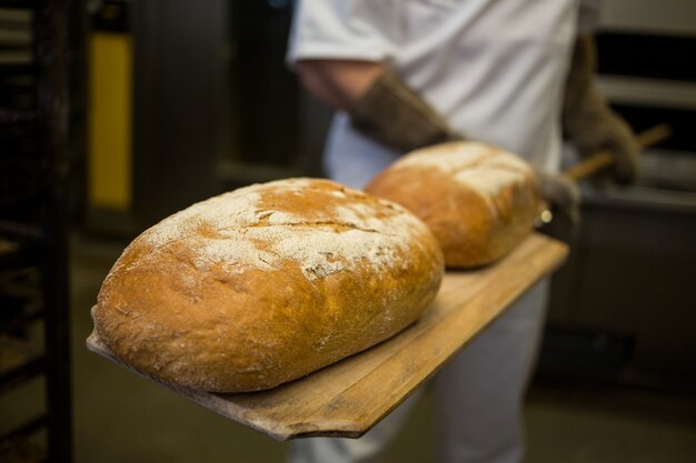 Baker removing baked buns from oven