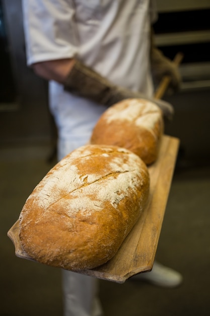 Baker removing baked buns from oven