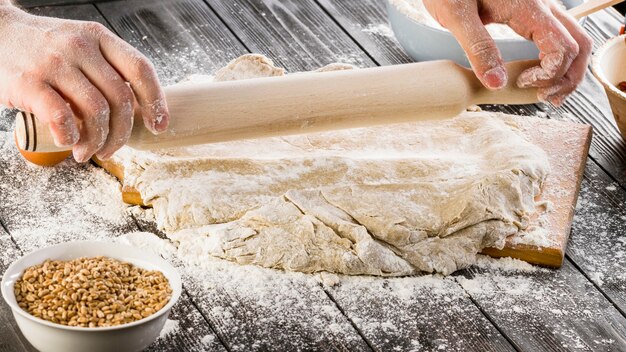 A baker rolling out the dough with wheat flour on chopping board