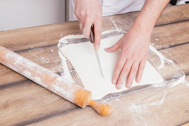 Baker's hand cutting the dough with sharp knife on wooden table