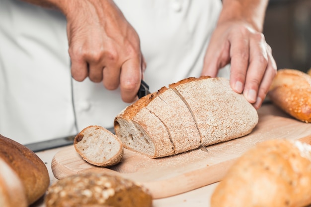 Baker's hand cutting fresh bread with knife