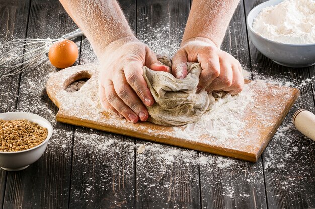 Baker's hand kneading dough with flour on chopping board