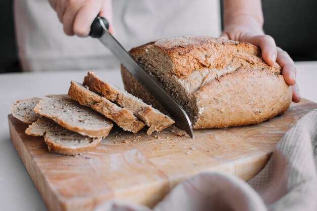 Baker's hand slicing loaf of fresh bread with knife