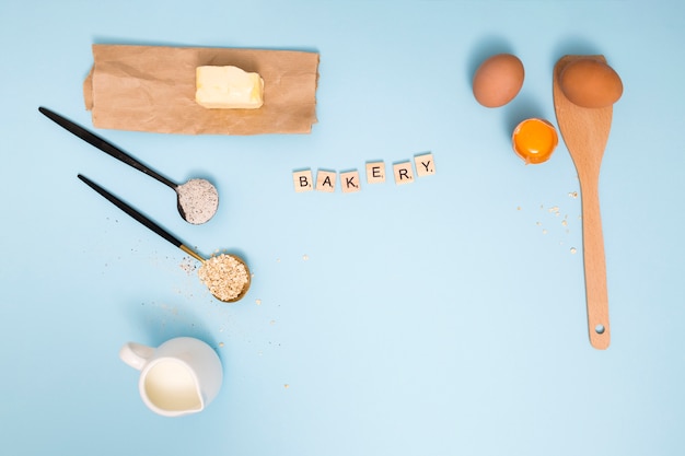 Free photo bakery blocks with butter; milk pitcher; oats barn; flour; eggs and wooden spatula on blue background