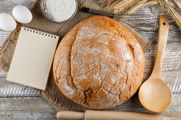 Bakery product with eggs, rolling pin, notepad, spoon, flour top view on a wooden surface