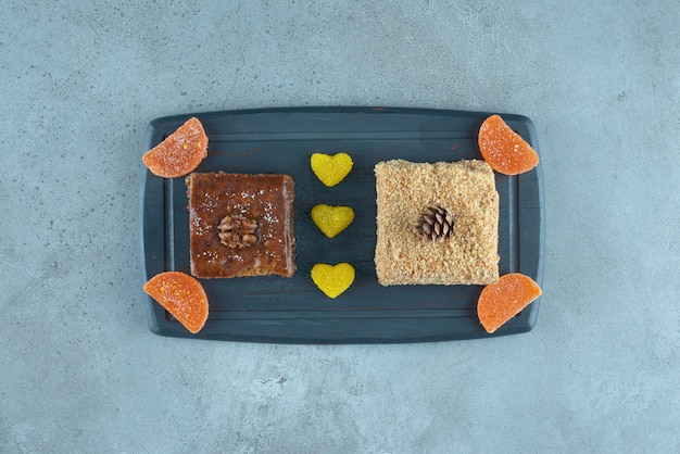 Free photo bakhlava, a slice of cake and some jelly candies on a navy board on marble surface