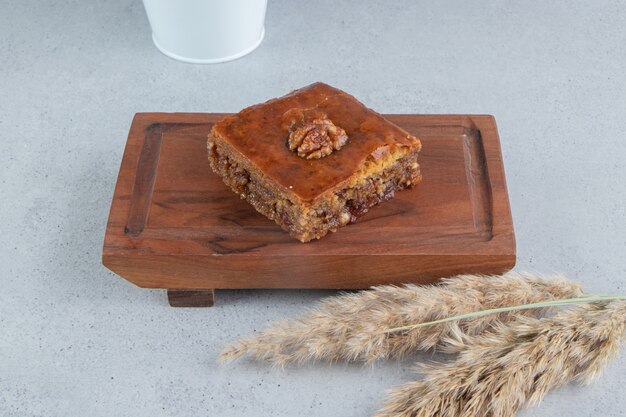 Bakhlava on a small board next to a bundle of feather grass stalks on marble background.