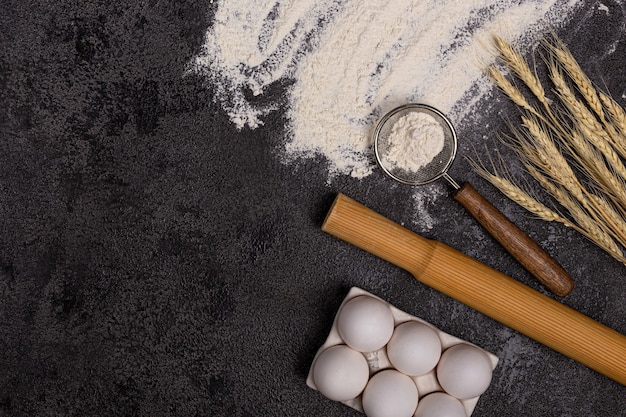 Baking background with free space for your text. flour in a bowl, eggs and wheat on a black table