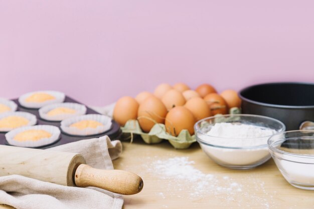 Baking cupcake ingredients with rolling pins on kitchen worktop against pink background