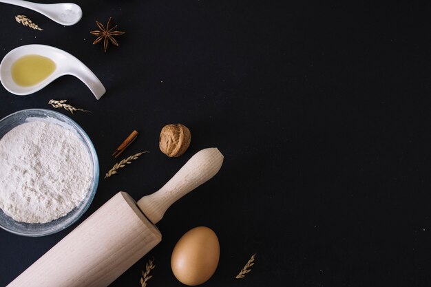 Baking ingredients and rolling pin on black background