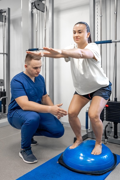 Esercizio di equilibrio con bosu ball donna e medico in palestra