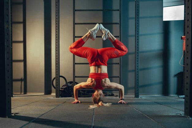 Сбалансированный. Молодая мускулистая кавказская женщина упражнениями в тренажерном зале. Спортивная (ый) женская модель делает силовые упражнения, тренирует нижнюю, верхнюю часть тела, растяжку. Велнес, здоровый образ жизни, бодибилдинг.