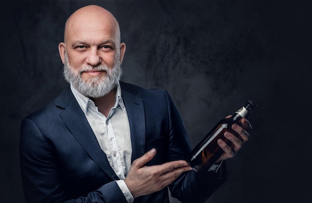 Free photo bald elderly man with grey beard and bottle posing against dark background.