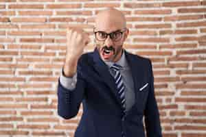 Free photo bald man with beard wearing business clothes and glasses angry and mad raising fist frustrated and furious while shouting with anger rage and aggressive concept