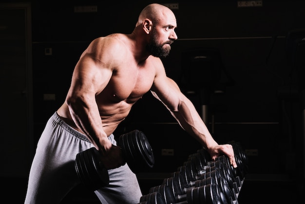 Bald man with dumbbell near rack