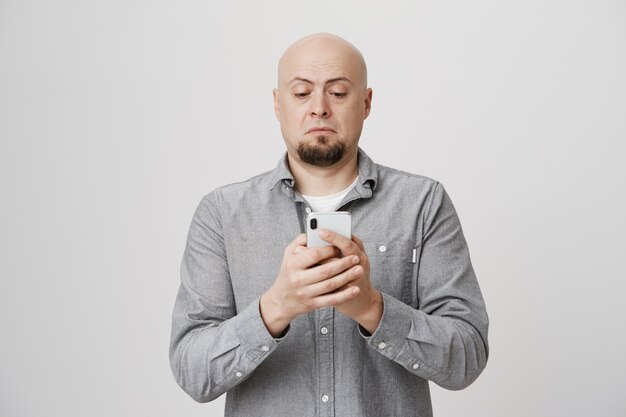 Bald middle-aged guy looking at phone without glasses