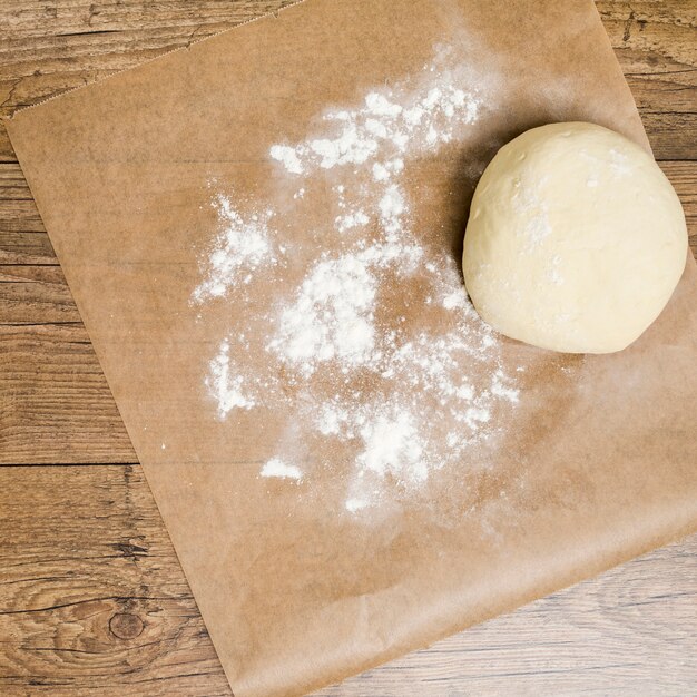 木製の背景上のほこりの小麦粉と羊皮紙紙の上の生地のボール