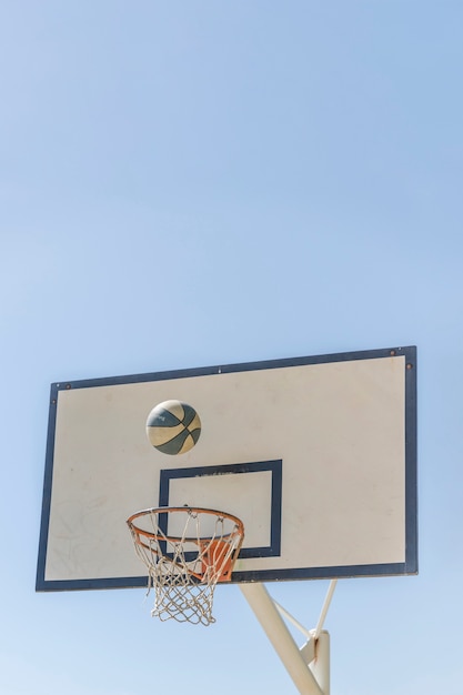 クリアな空に対してバスケットボールのフープに落ちるボール