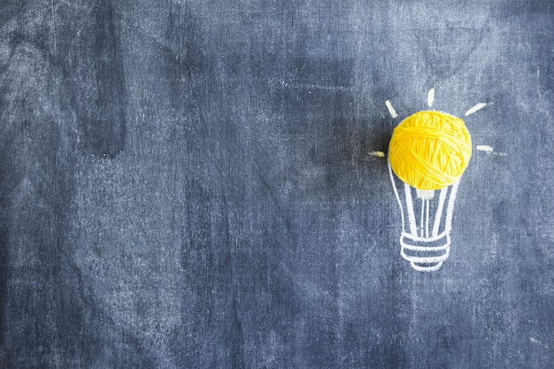 Ball of yellow wool over the hand drawn light bulb on chalkboard