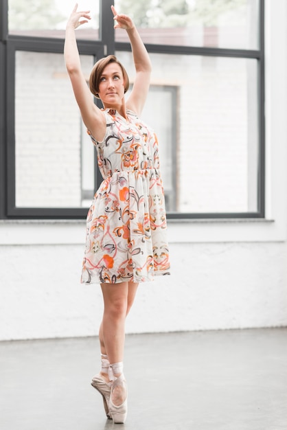 Free photo ballerina in floral dress posing on pointe shoes