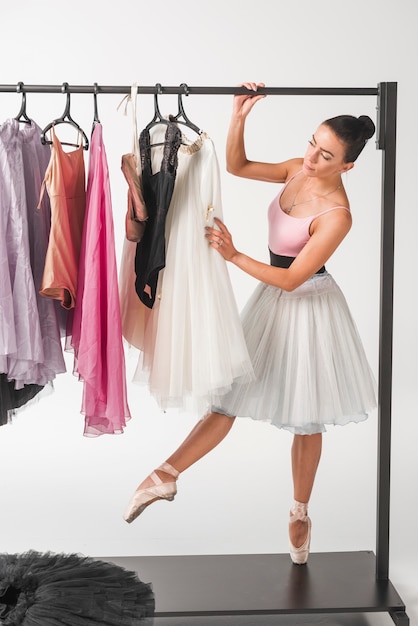 Балерина, стоя на цыпочках, выбирая пачку из вешалок на белом фоне