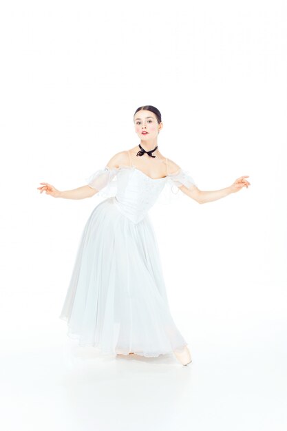 Ballerina in white dress posing on pointe shoes, studio white.