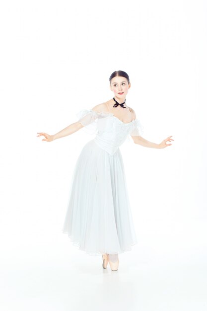 Балерина в белом платье позирует на пуанты, студия белая.
