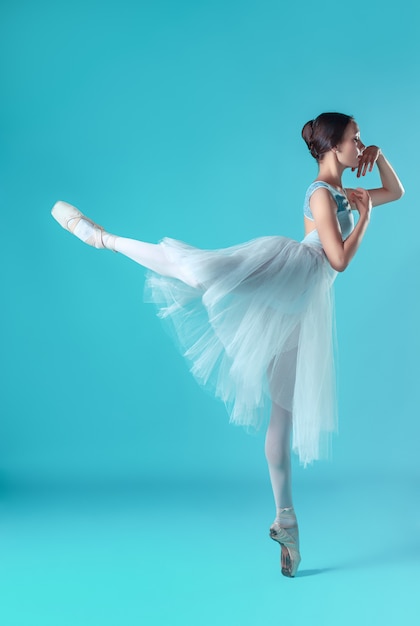 Ballerina in white dress posing on toes, studio background.