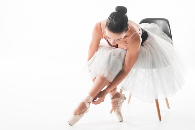 Ballet dancer sitting on chair tying ballet shoes against white background