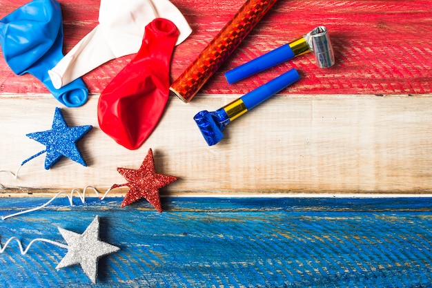 Balloons; sparkling stars; party horn and firecracker on painted wooden backdrop