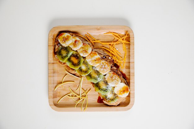 Banana and kiwi slices with sauce inside bamboo plate.