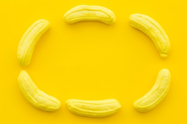 Banana shaped candies forming frame on yellow background