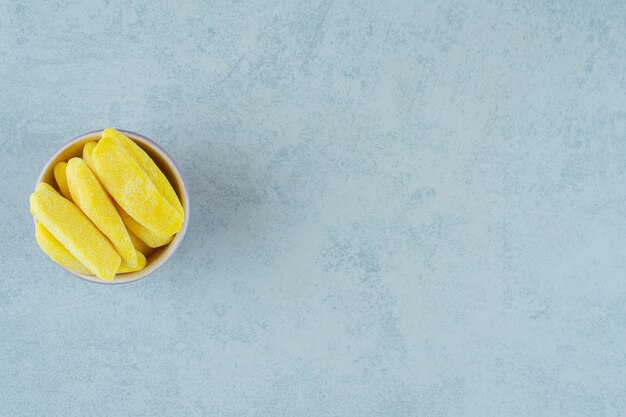 Banana shaped chewing candies in bowl on white surface