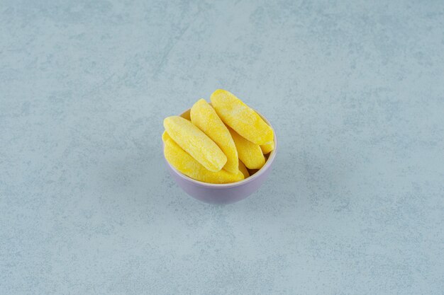 Banana shaped chewing candies in bowl on white surface