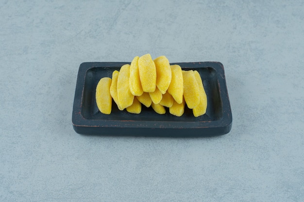 Banana shaped chewing candies in a wooden board on white surface