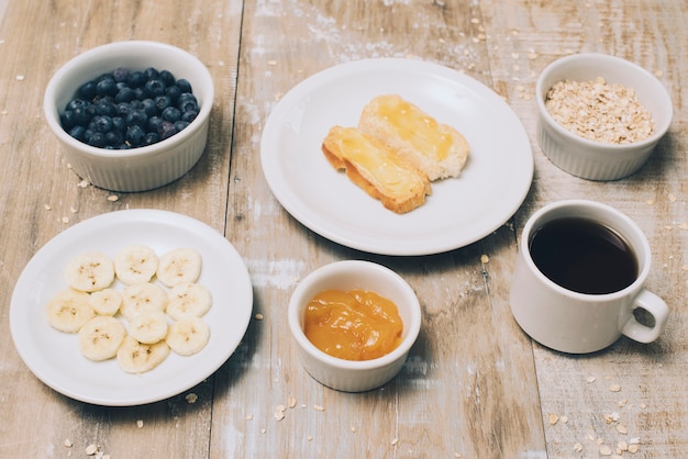バナナのスライスジャム;ブルーベリー;オート麦と木製のテーブルの上のコーヒーカップ