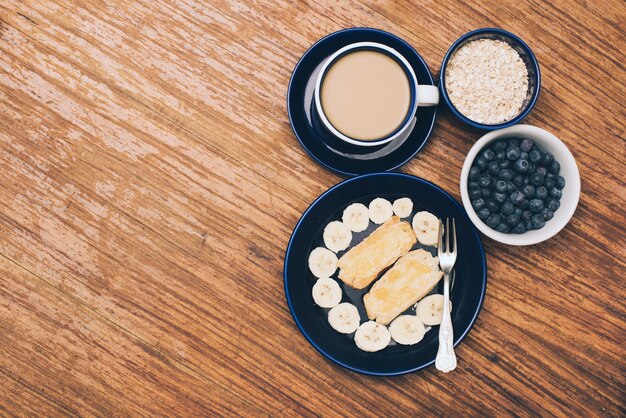 바나나; 토스트 빵; 블루 베리; 나무 질감 배경 muesli와 커피 컵
